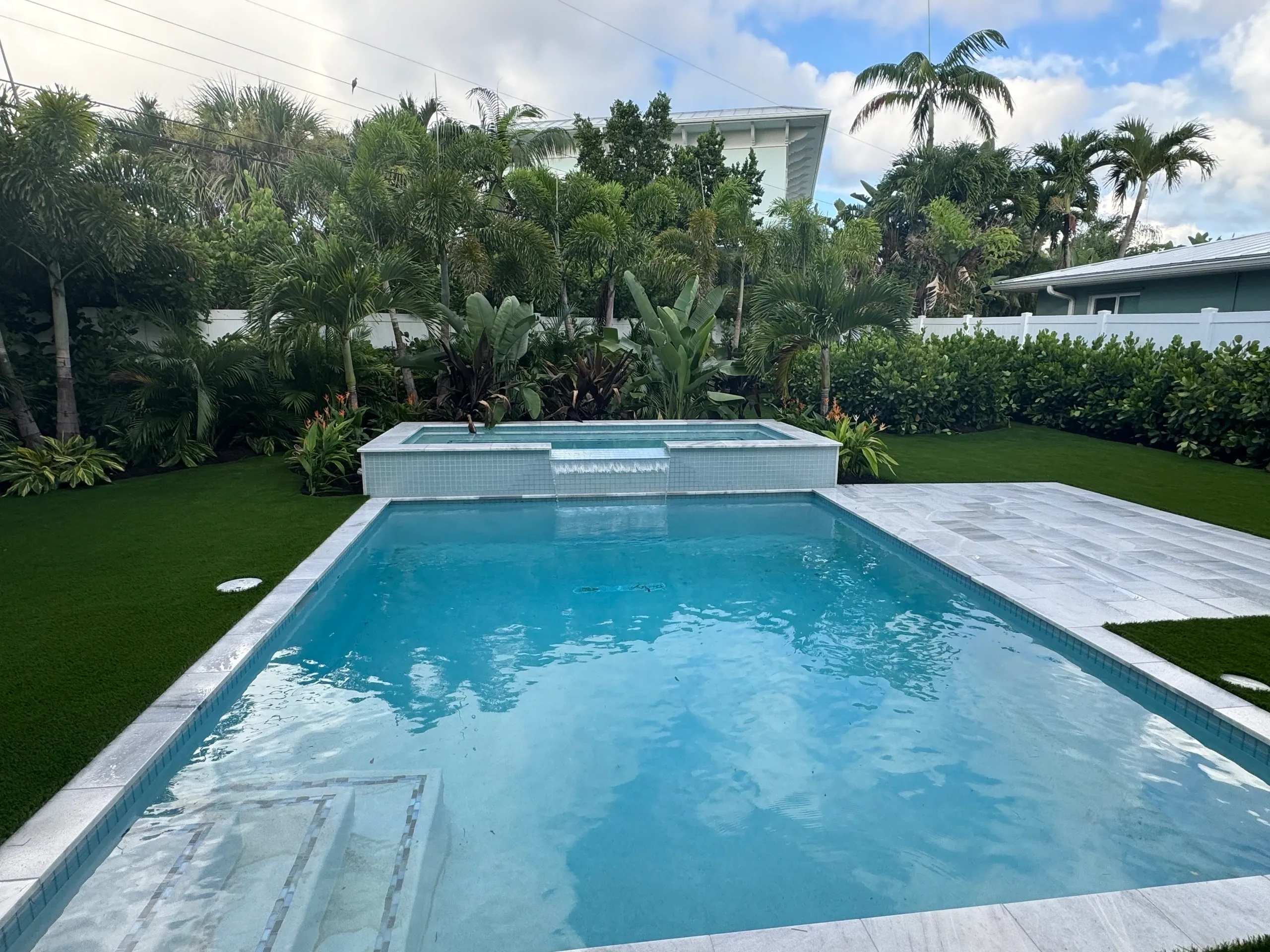 Luxurious pool surrounded by lush tropical landscaping, featuring a spa area, vibrant greenery, and modern paver stones, ideal for enhancing outdoor spaces.